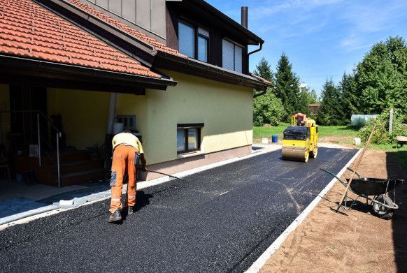 A man is laying asphalt on a driveway in front of a house.