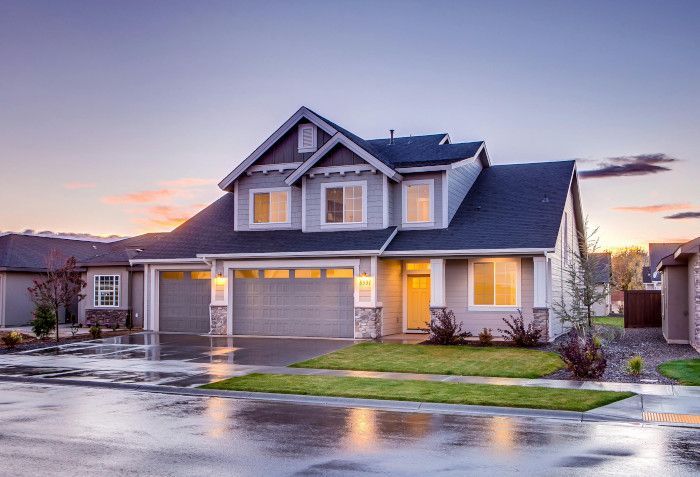 A large house is sitting on top of a lush green lawn on a rainy day.