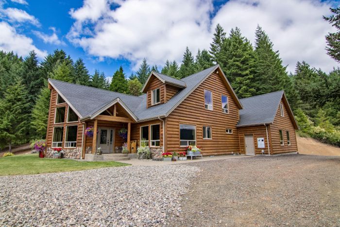 A large log cabin in the middle of a forest. It has a gravel driveway in the process of being paved by Cornflower Driveways.