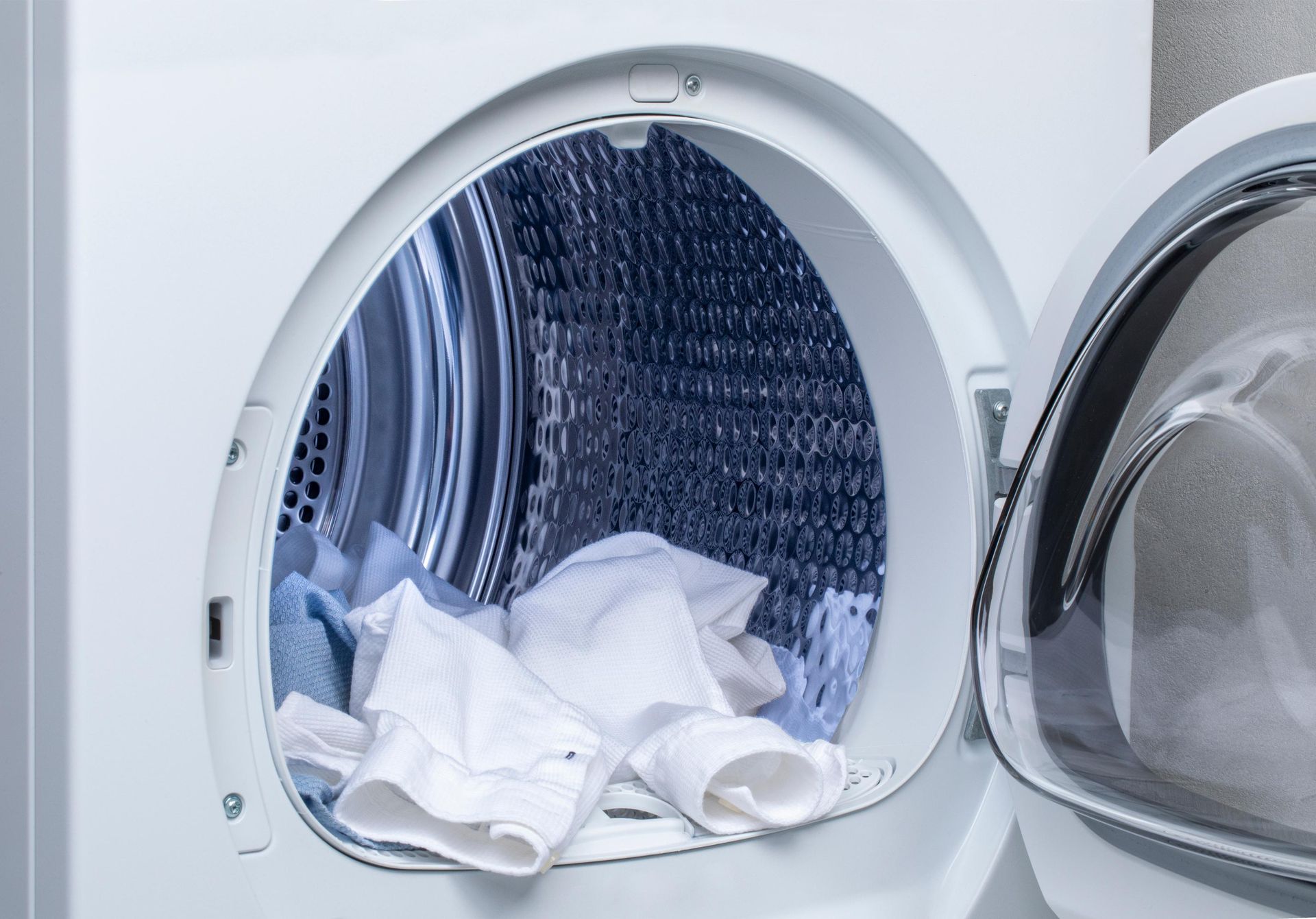 Open washing machine door with white and blue clothes inside.