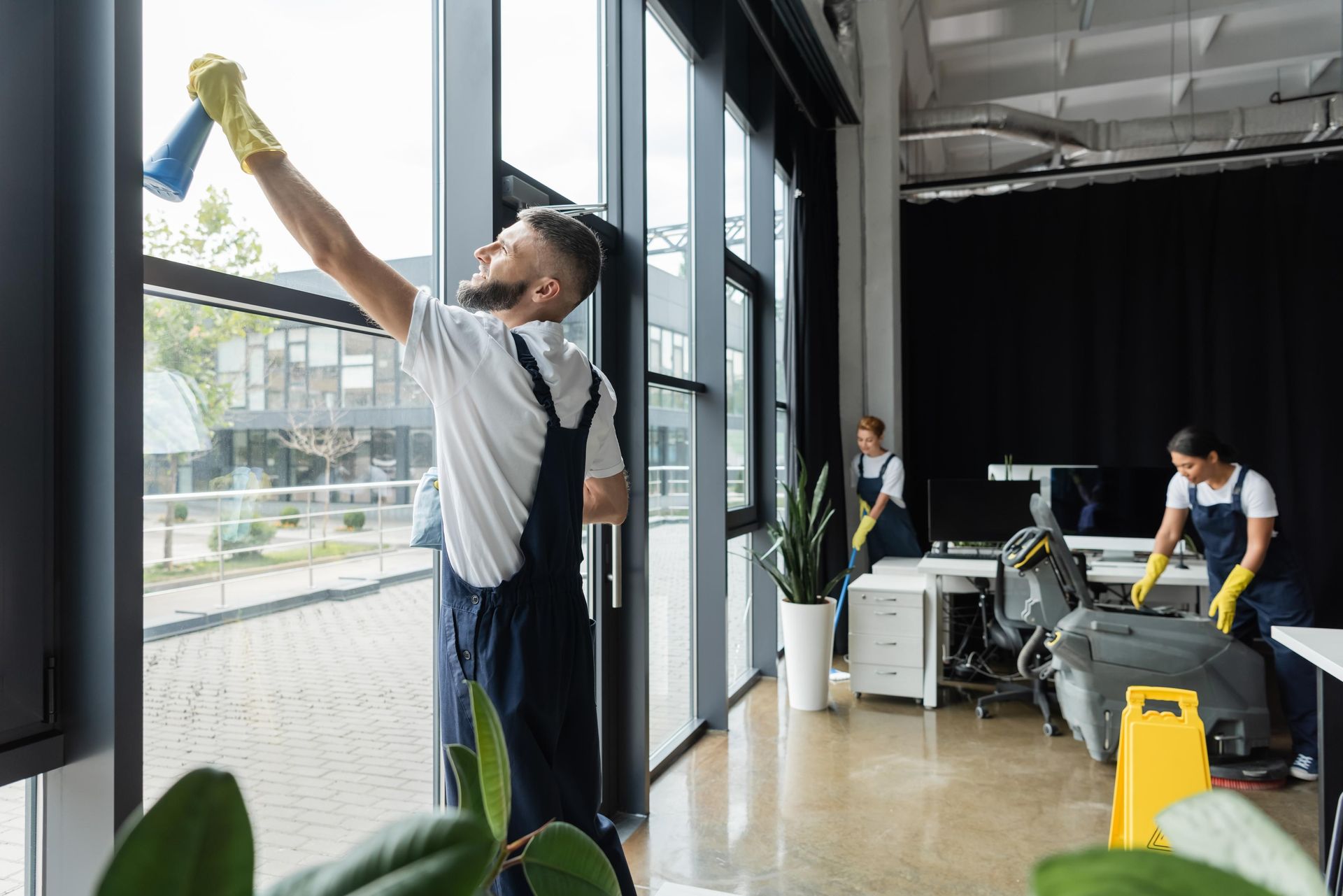 Cleaning crew in an office, one wiping a window, two others cleaning near desks.