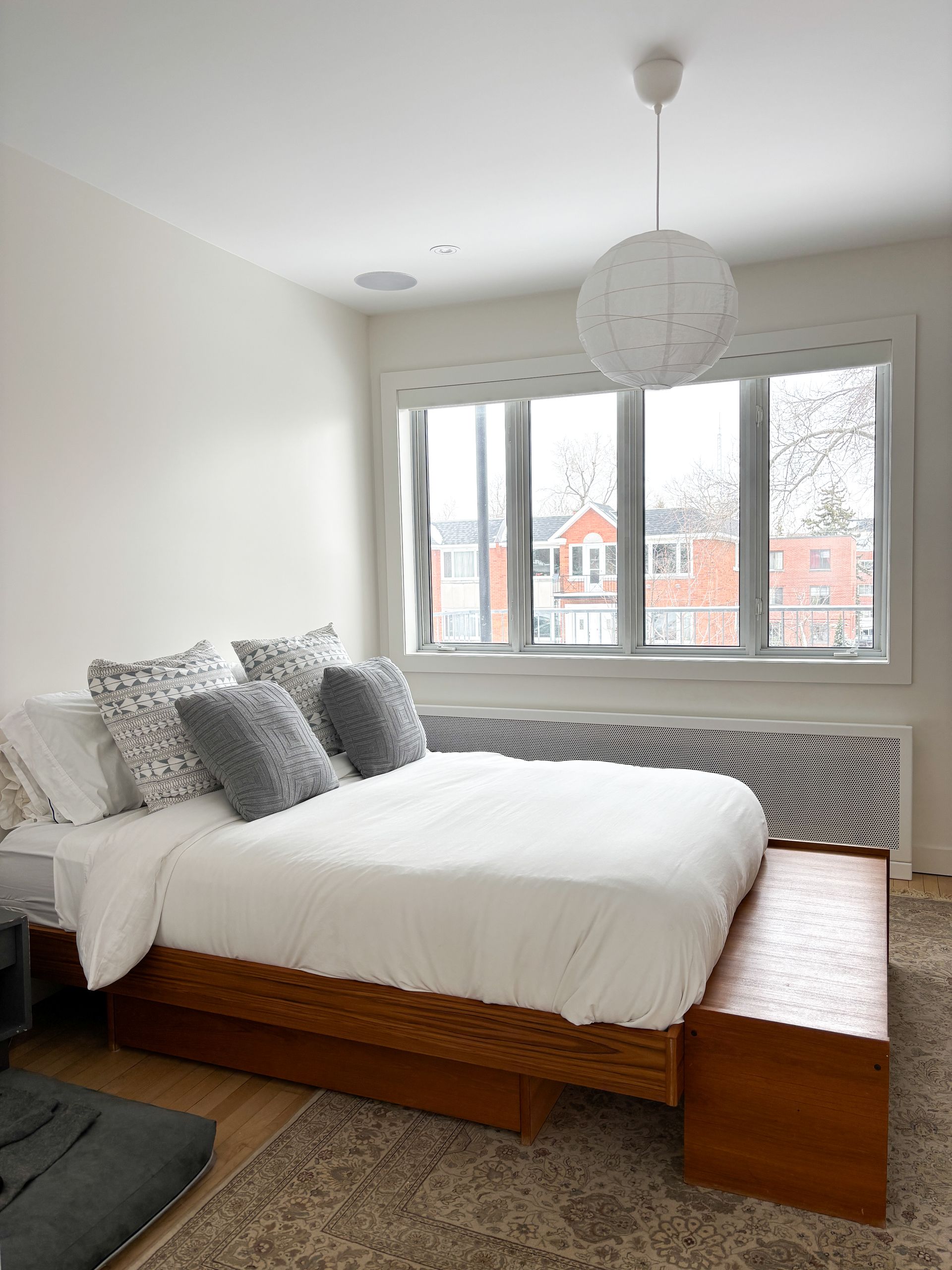 Chambre avec un lit, une grande fenêtre, une suspension et un radiateur.