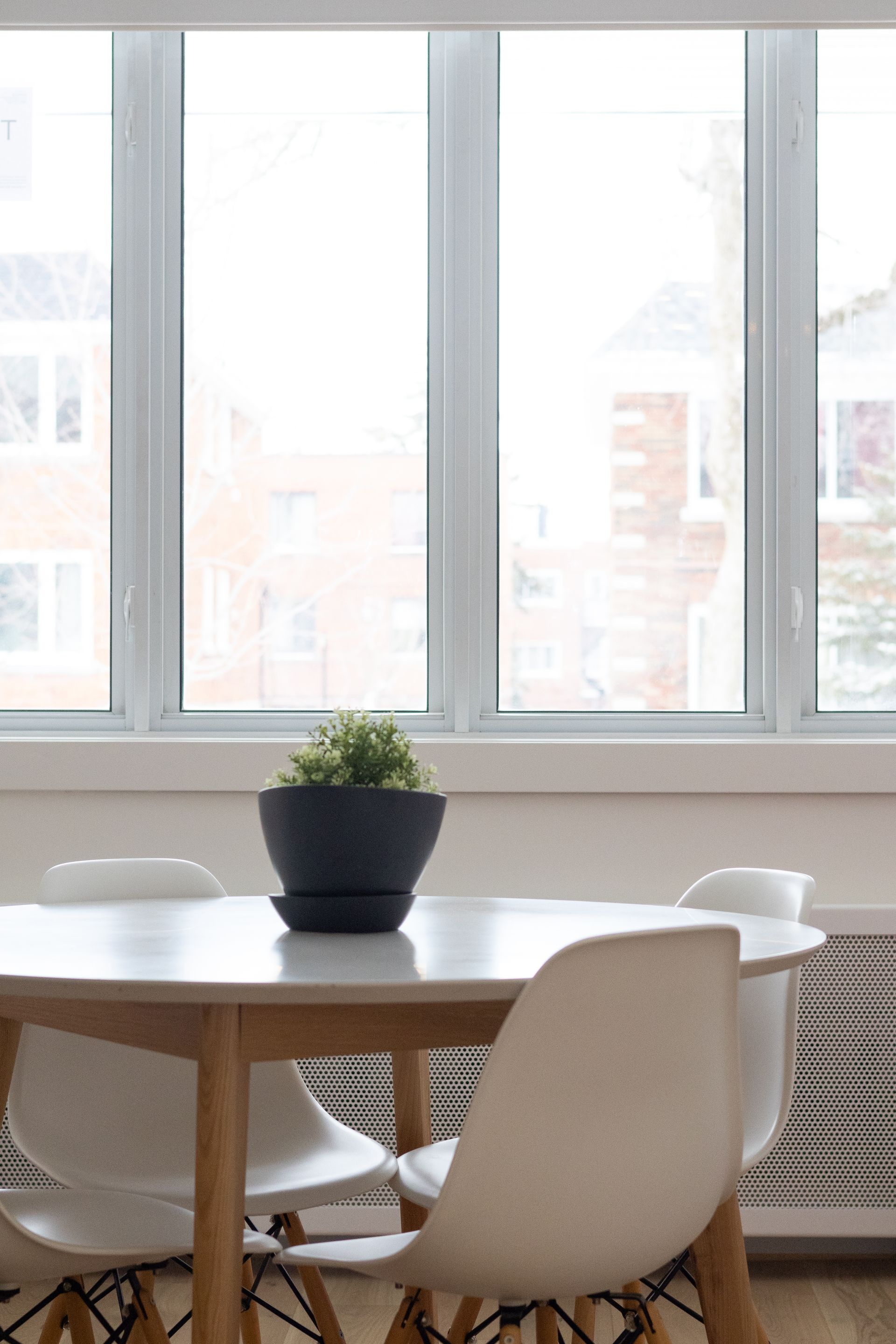 Table blanche avec quatre chaises, une plante en pot devant une fenêtre.