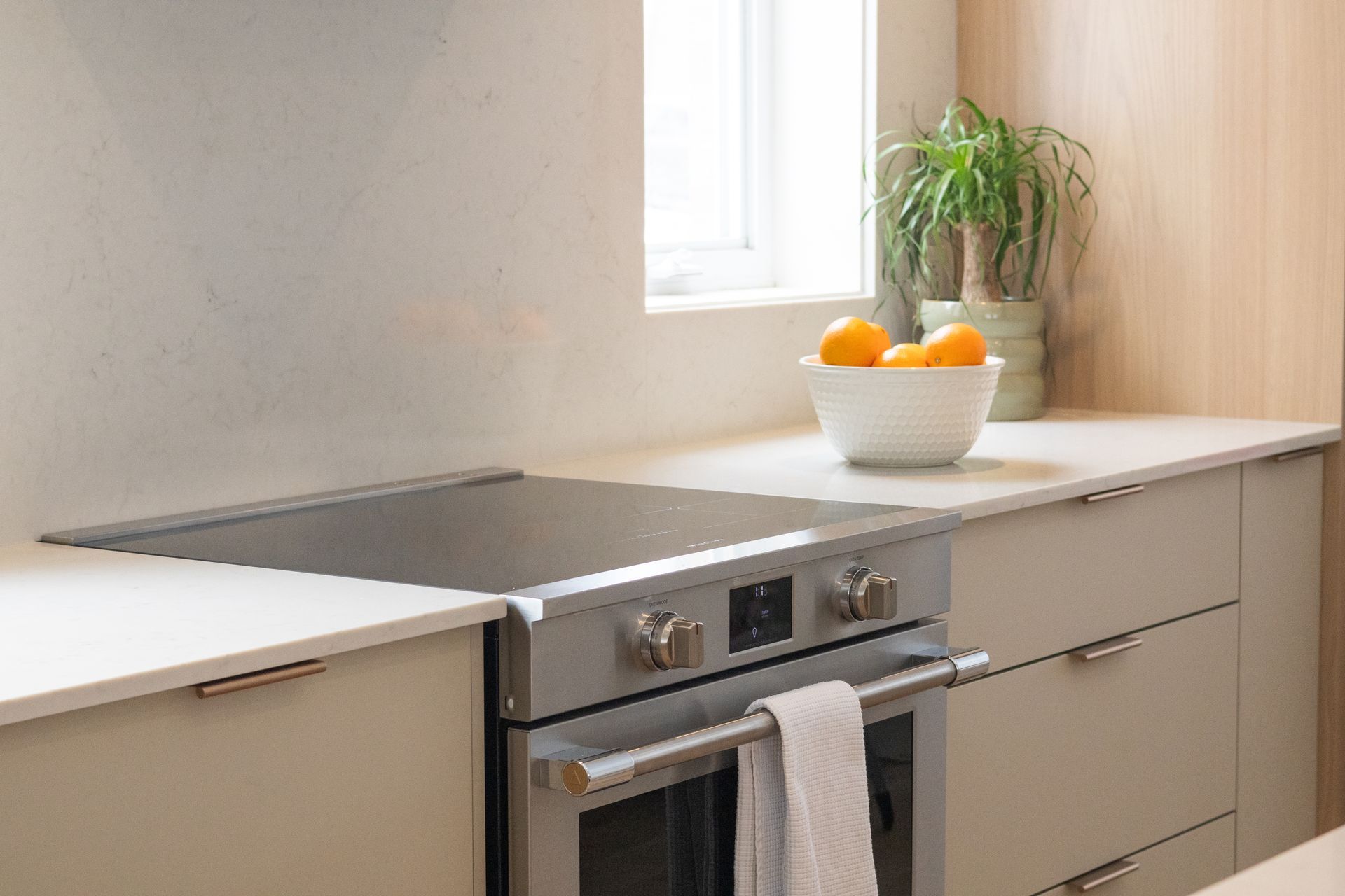 Cuisine moderne avec four et plaque de cuisson intégrés en inox. Oranges dans un bol blanc et plante sur le plan de travail.