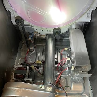 Internal view of an open clothes dryer showing the motor, heating element assembly, wiring, and metal exhaust duct.