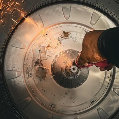 A person uses a power tool to cut the metal base of a washing machine tub, creating sparks.