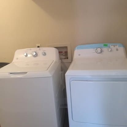 A white top-loading washing machine sits next to a white clothes dryer in a laundry room.