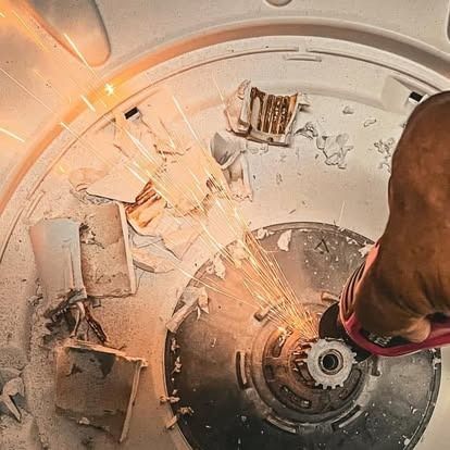 An angle grinder cuts through metal inside a washing machine tub, creating sparks.