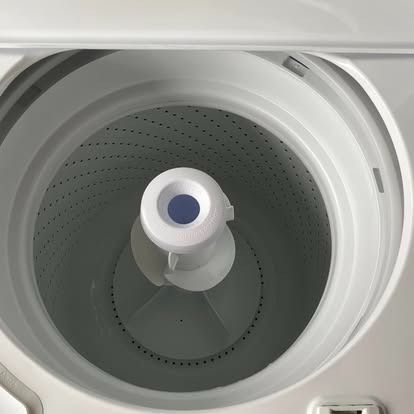 The interior of a white top-load washing machine with a central agitator, viewed from above.
