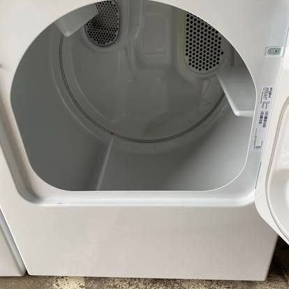 The open door of a white clothes dryer, showing the interior drum and metal vents.