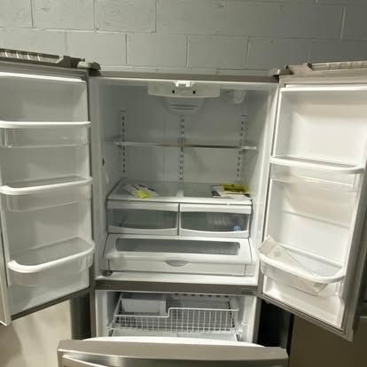 The open, empty interior of a stainless steel refrigerator with multiple shelves, storage drawers, and door bins.