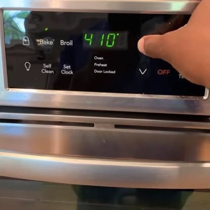 A hand presses a button on a stainless steel oven control panel displaying 410 degrees.