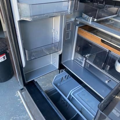 Interior of an open, empty stainless-steel refrigerator showing glass shelves, door bins, and a bottom pull-out freezer.