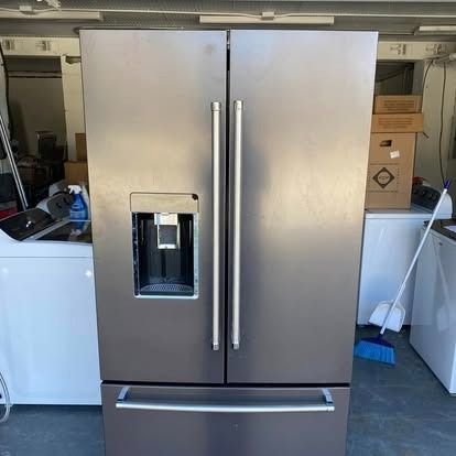 A stainless steel French door refrigerator with an external water and ice dispenser, standing in a garage.