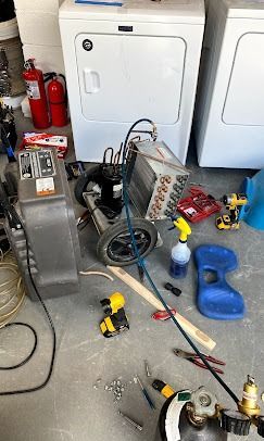 A floor-level view of a dehumidifier repair in progress, featuring tools, a gas cylinder, and parts on a laundry room floor.