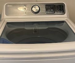 Top-loading white Midea washing machine with a glass lid and a control panel featuring a center dial and digital display.