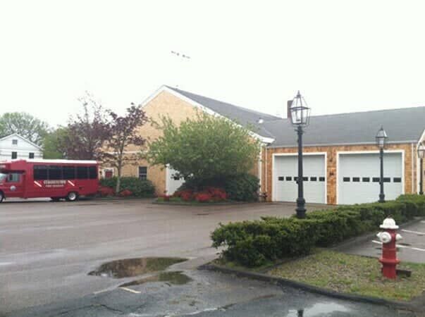 A brick fire station with white garage doors, a red bus parked in front, and a fire hydrant in the foreground.