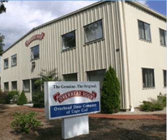 A light-colored industrial building with a sign for the Overhead Door Company of Cape Cod in the foreground.