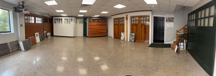 A showroom interior displaying various garage door styles, colors, and designs, with a seating area to the right.