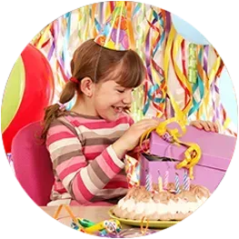 A little girl wearing a party hat is opening a gift box at a birthday party.