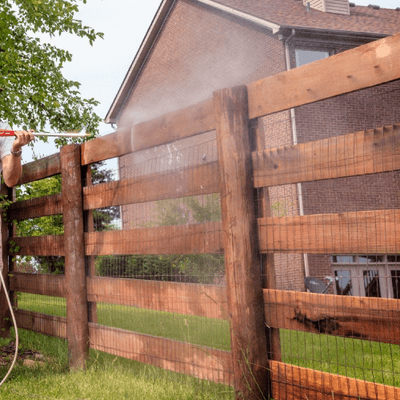 A person is spraying a wooden fence with a hose.