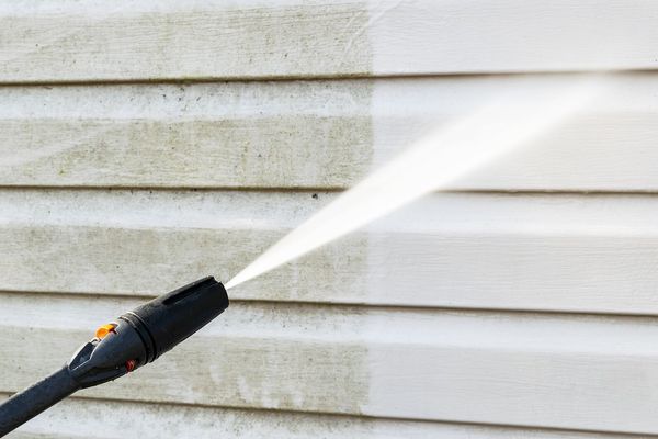 A person is using a high pressure washer to clean the side of a house.