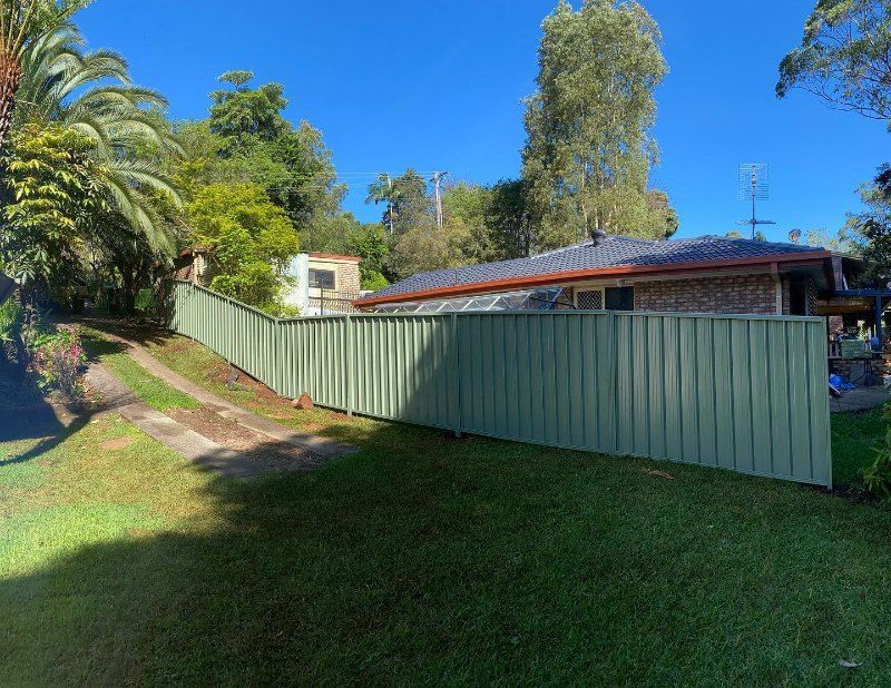 A Green Fence Surrounds a House in a Lush Green Yard — Fence & Deck Australia Pty Ltd in Balina, NSW