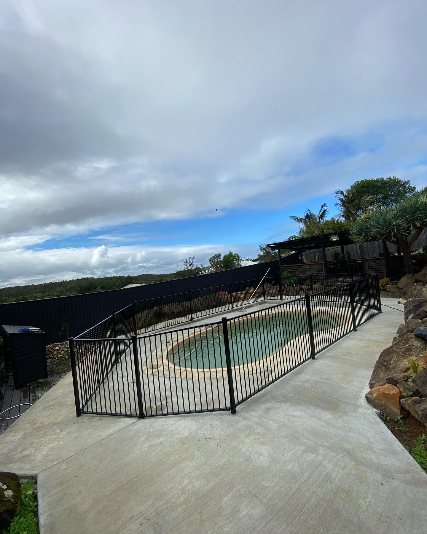 A Swimming Pool Surrounded by a Fence on a Cloudy Day — Fence & Deck Australia Pty Ltd in Pottsville, NSW