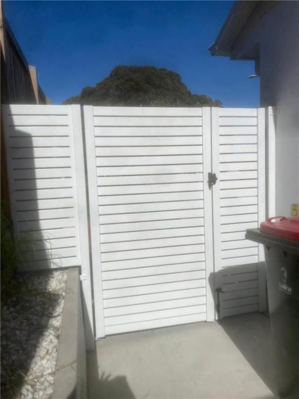 A White Fence With a Red Trash Can in Front of It — Fence & Deck Australia Pty Ltd in Brunswick Heads, NSW