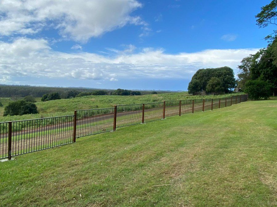 A Fence Surrounds a Grassy Field With Trees in the Background — Fence & Deck Australia Pty Ltd in Casino, NSW