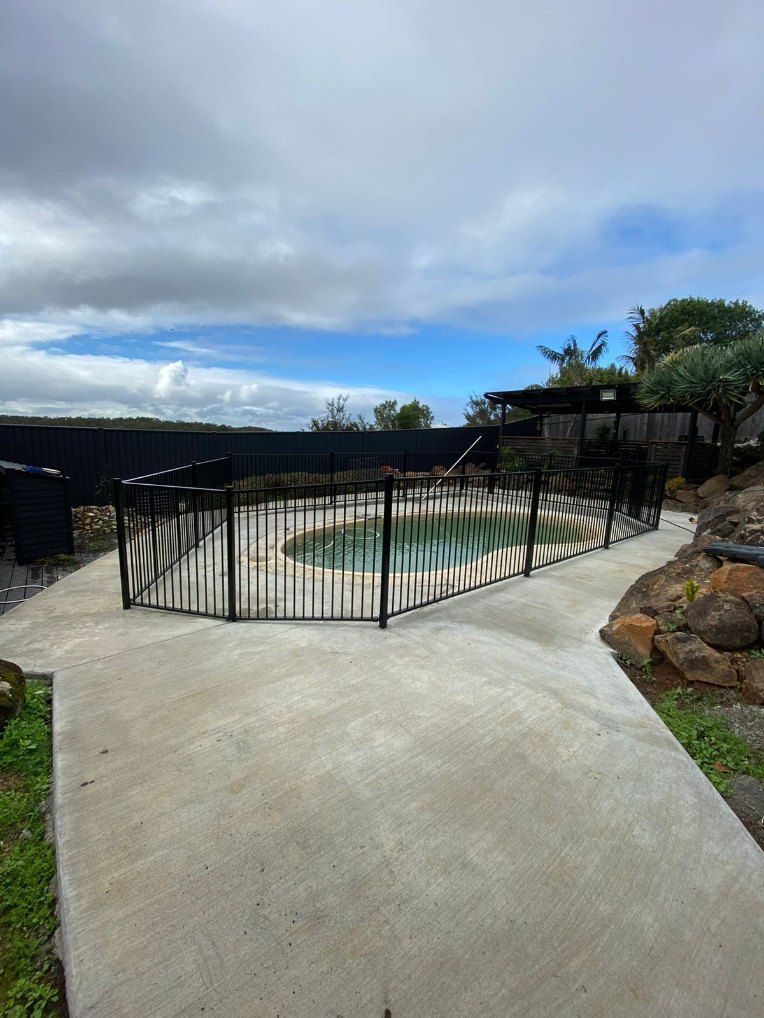 A Swimming Pool Surrounded by a Metal Fence and a Concrete Walkway — Fence & Deck Australia Pty Ltd in Casino, NSW