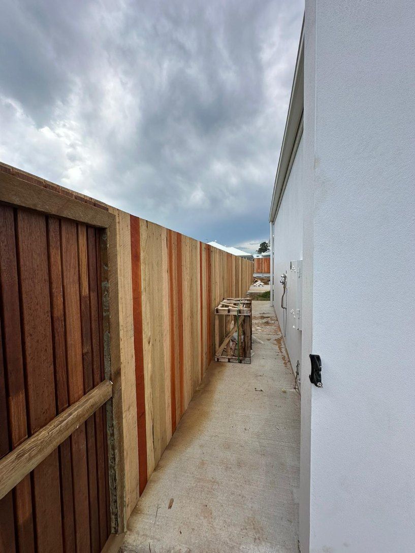 There is a Wooden Fence Between Two Buildings — Fence & Deck Australia Pty Ltd in Casino, NSW