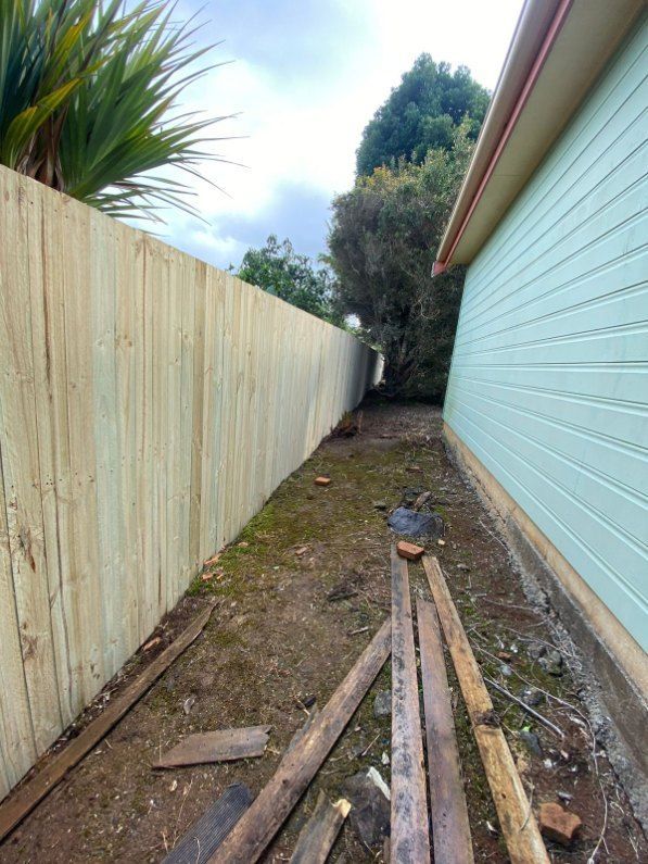 A House With a Wooden Fence and a Pile of Wood in Front of It — Fence & Deck Australia Pty Ltd in Casino, NSW