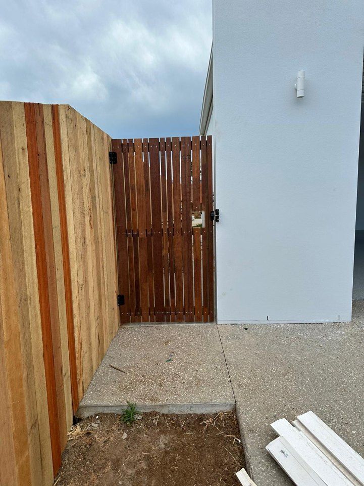 There is a Wooden Fence and a Wooden Gate in Front of a White Building — Fence & Deck Australia Pty Ltd in Casino, NSW