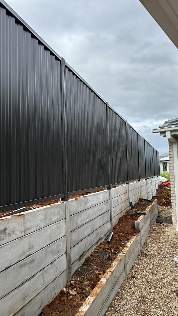 A Black Fence is Sitting Next to a Concrete Wall — Fence & Deck Australia Pty Ltd in Casino, NSW