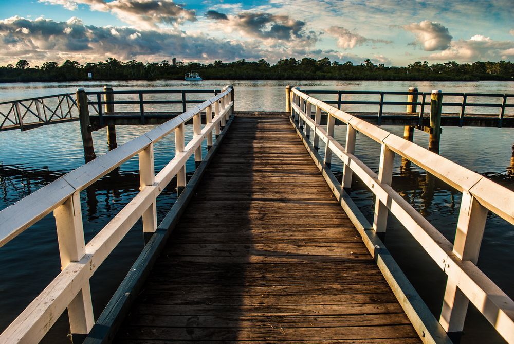 A Wooden Dock Leading to a Body of Water With a White Railing — Fence & Deck Australia Pty Ltd in Tweet Heads, NSW