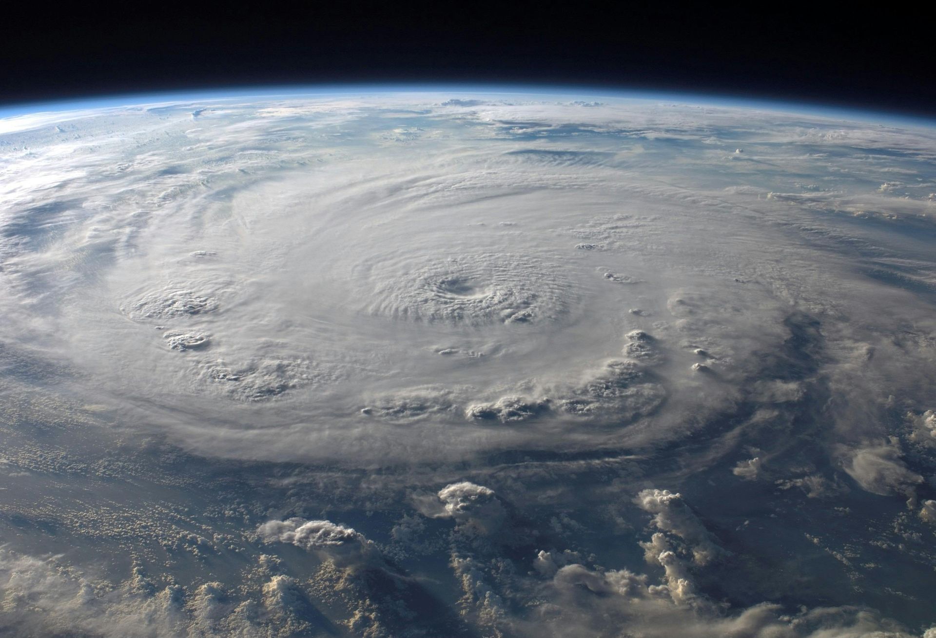 A hurricane, a swirling vortex of white clouds, viewed from space over Earth's curvature.
