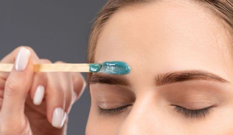 A woman is waxing her eyebrows with a stick.