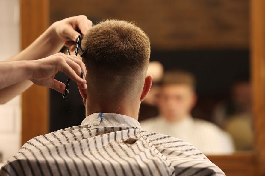 A man is getting his hair cut by a barber in front of a mirror.