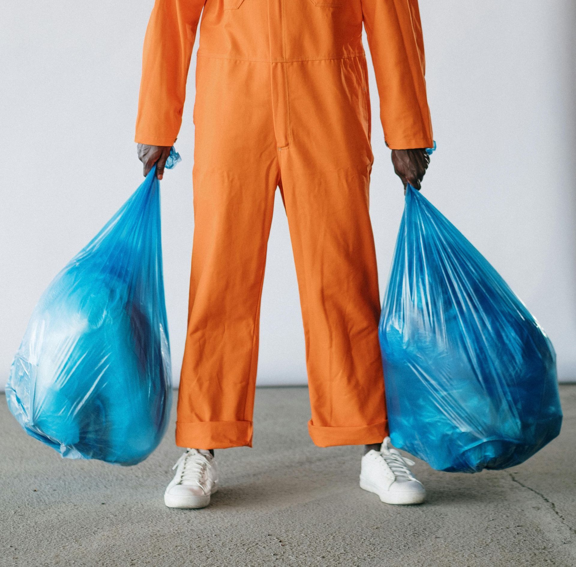 Persoon met oranje overal en 2 blauwe vuilniszakken