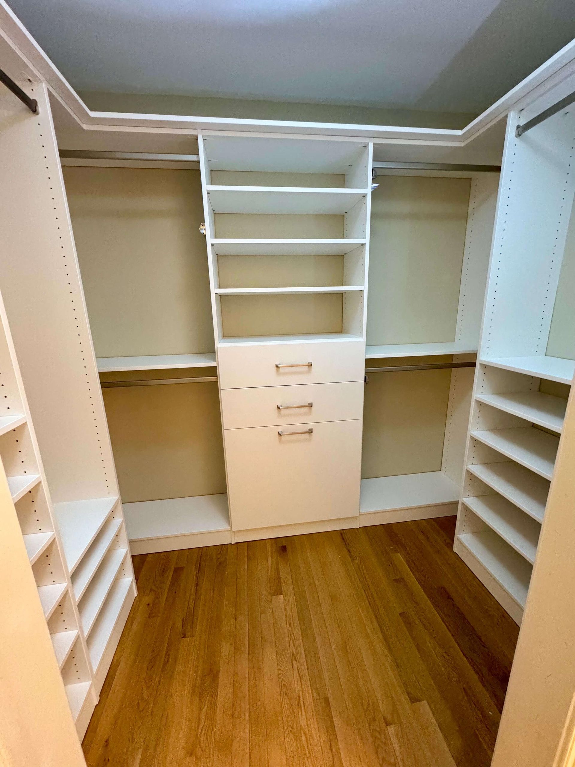 A walk in closet with wooden floors and white shelves.