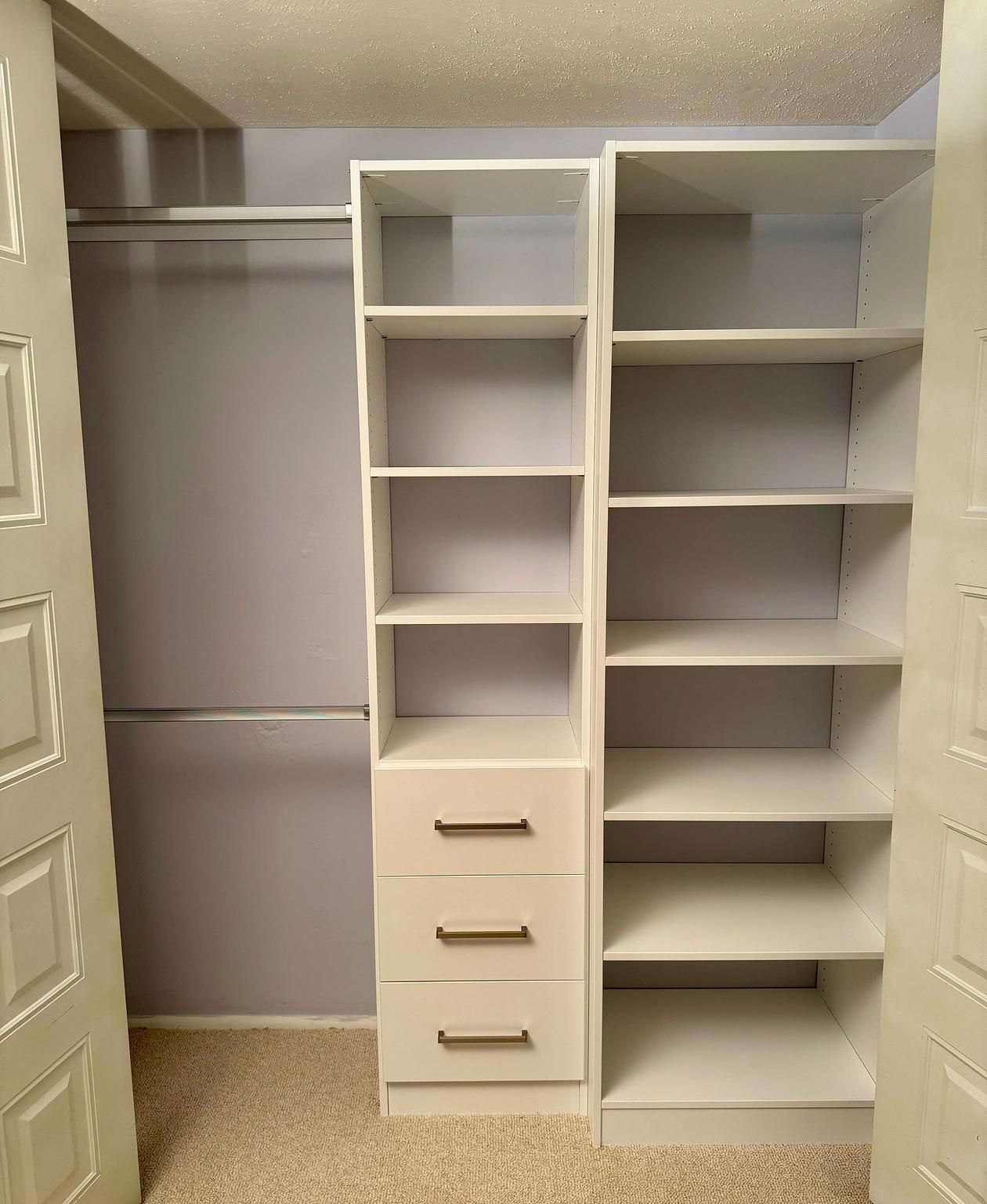 A walk in closet with lots of shelves and drawers and a blue ottoman.