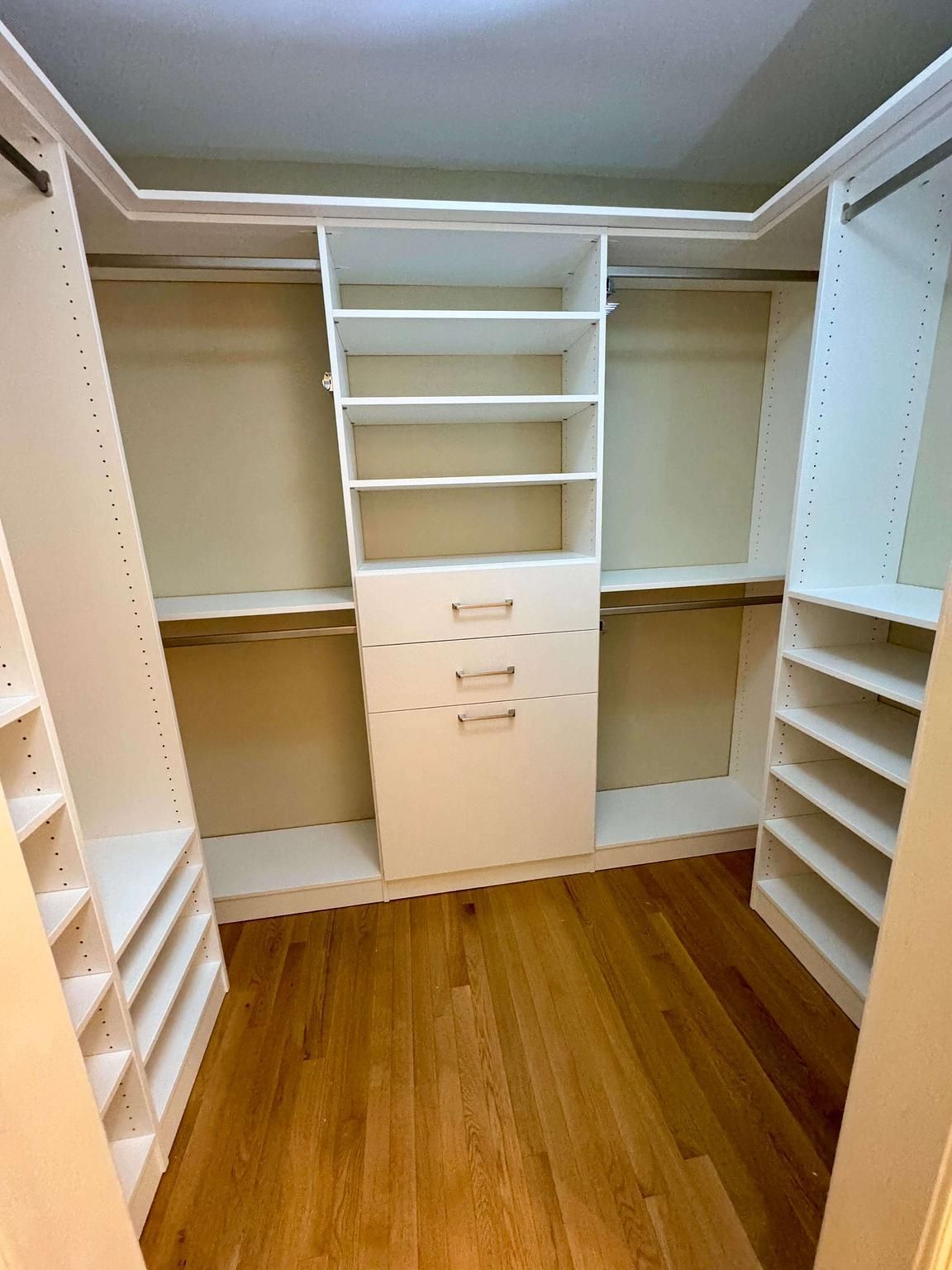 A walk in closet with wooden floors and white shelves.