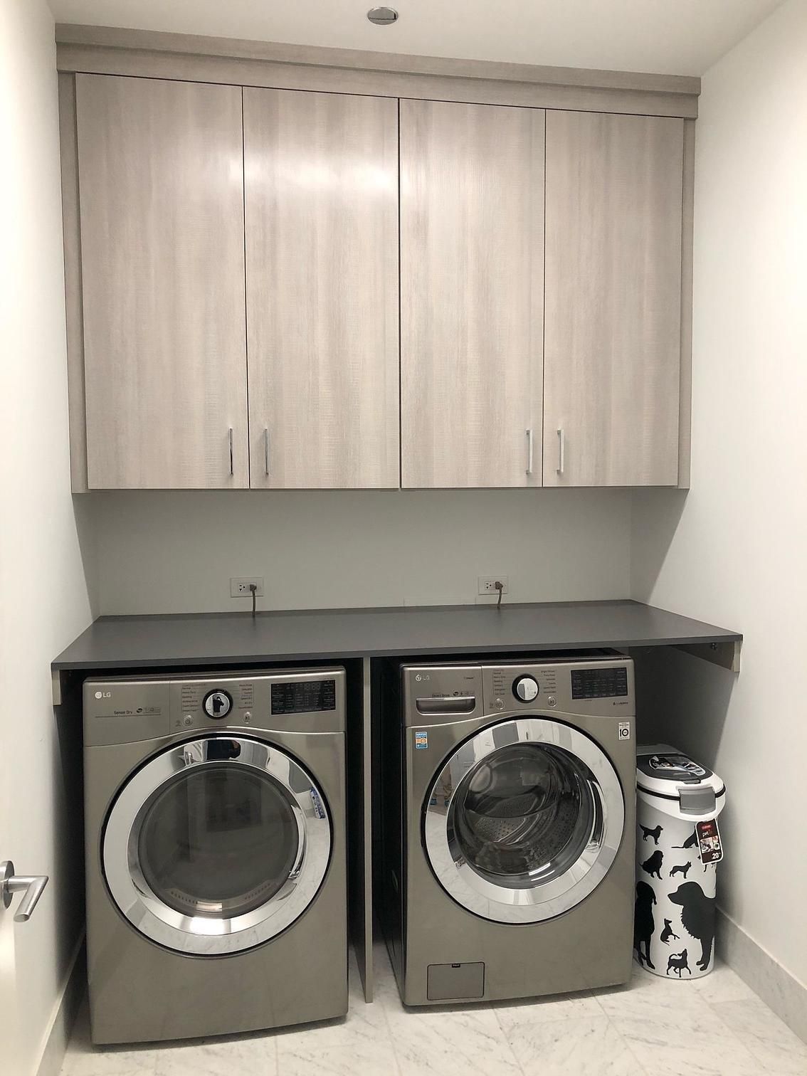 A laundry room with two washing machines and a trash can.
