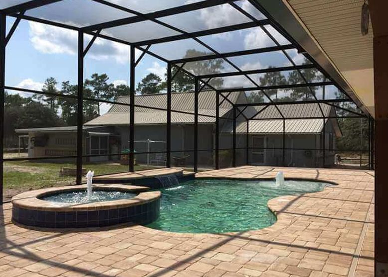 A swimming pool with a fountain in the middle of it is surrounded by a screened in area.