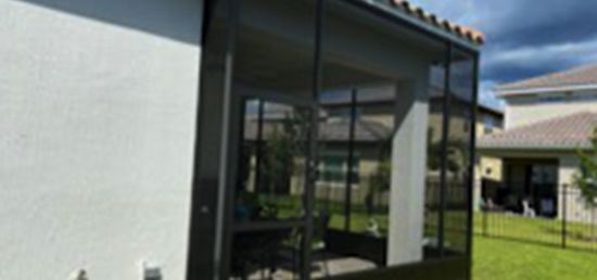 A screened in porch with a white house in the background.