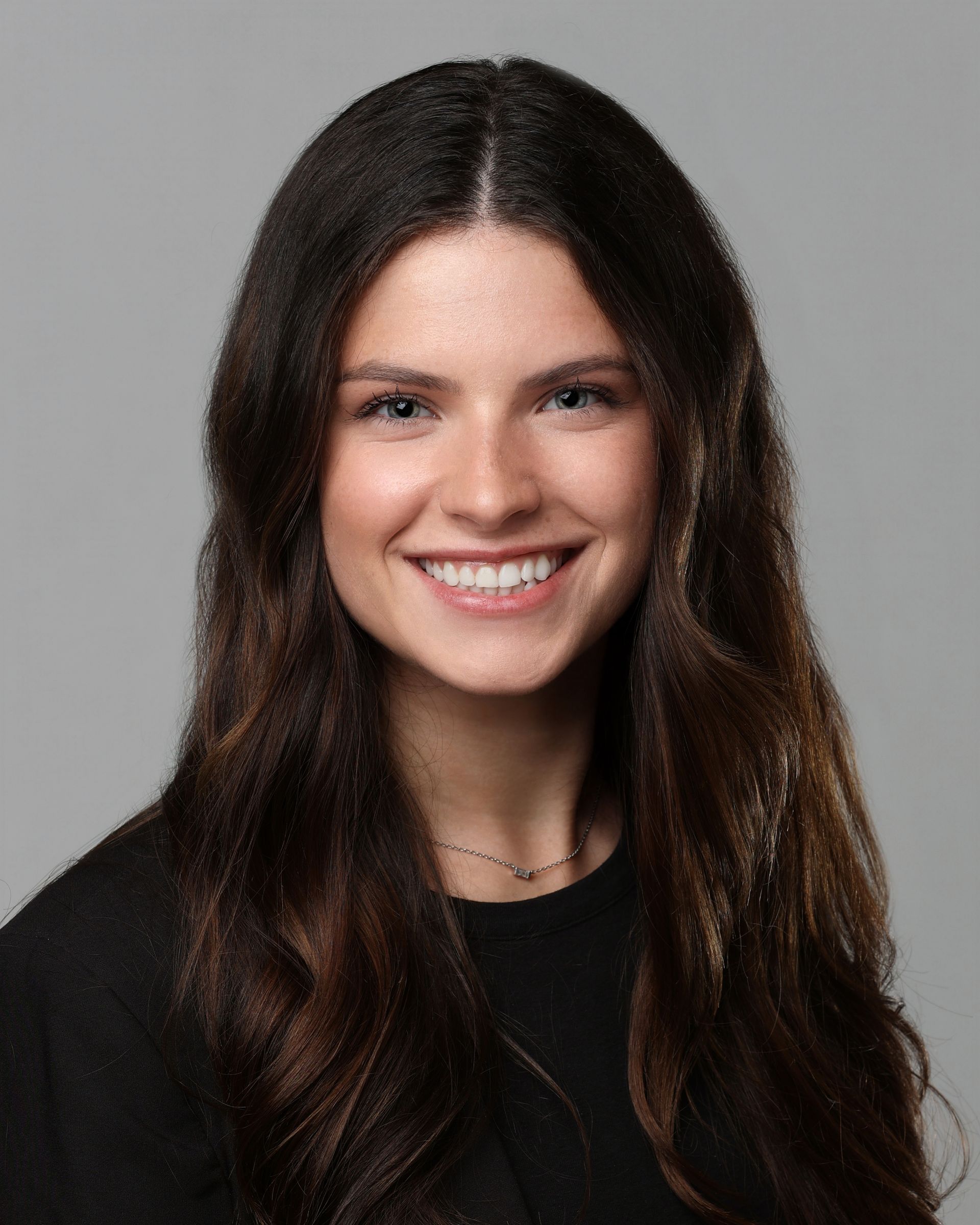 A woman wearing glasses is smiling in front of a city street.