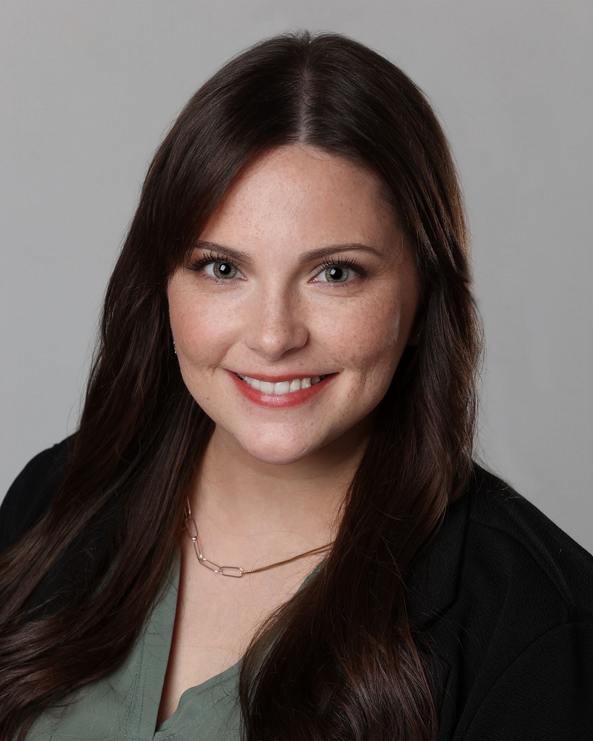 A woman with long red hair is standing in front of a tree and looking at the camera.