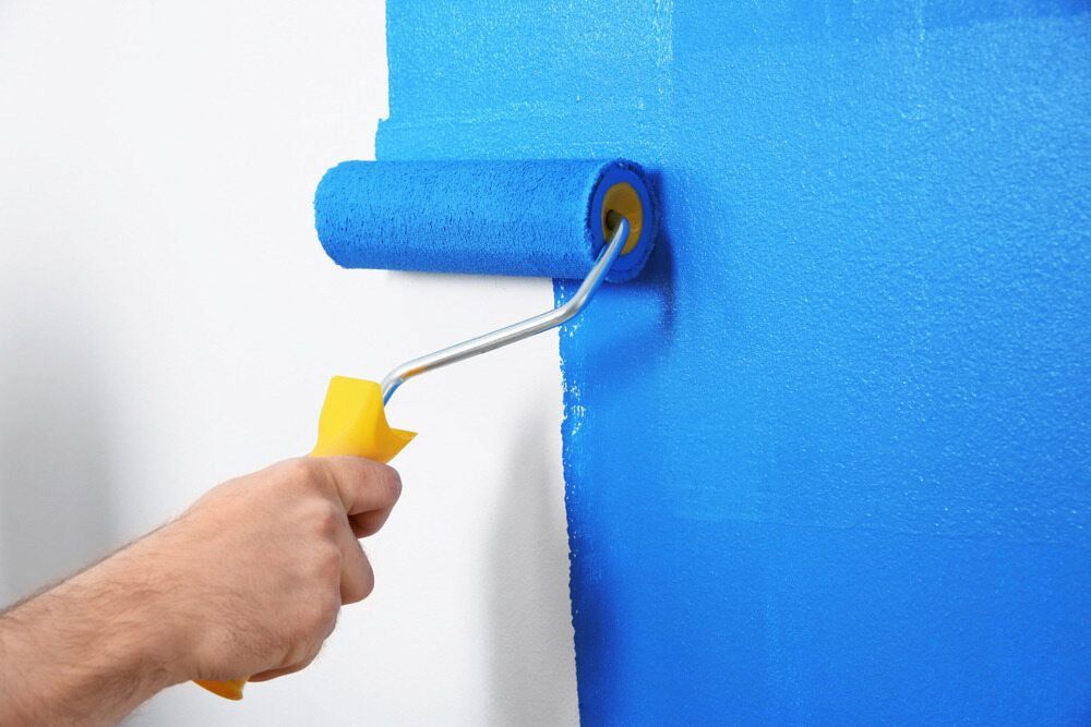 A Person Is Painting A Wall With A Blue Paint Roller — L & S Wirth Painting in Bourke, NSW