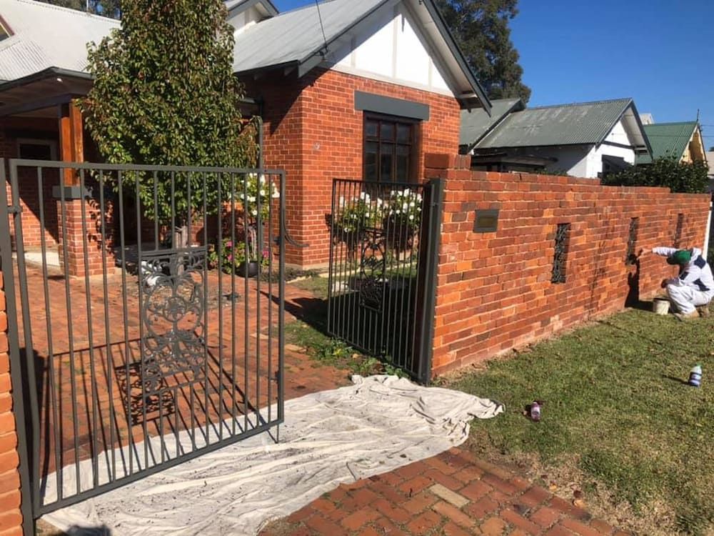 A Man Is Painting A Brick Wall In Front Of A House — L & S Wirth Painting in Dubbo, NSW
